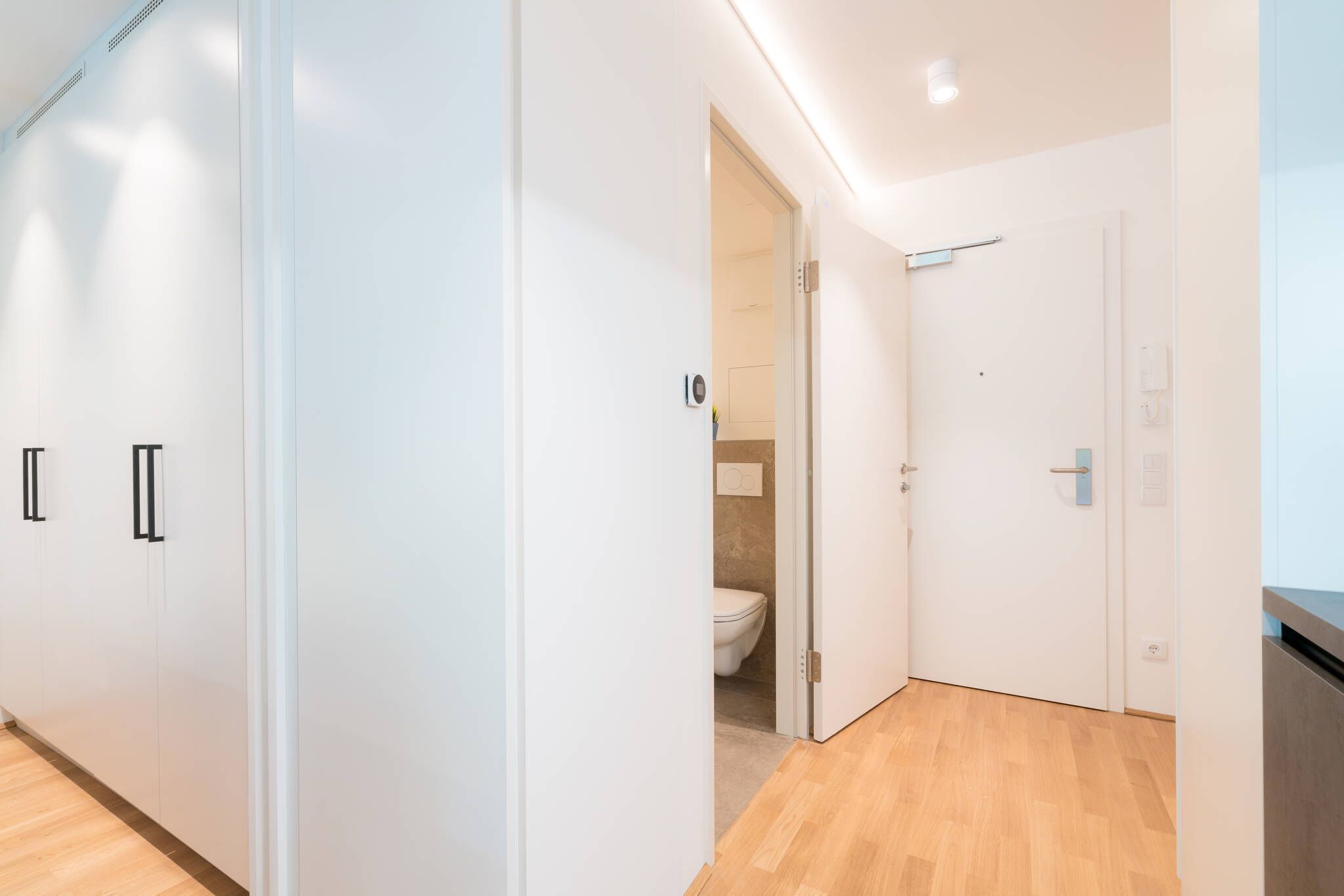 Une chambre d’hôtel moderne avec un plancher en bois, des murs blancs et une salle de bain ouverte équipée de toilettes et d’un lavabo.