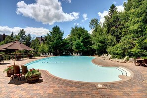 Une piscine entourée d’arbres et dotée d’une terrasse en briques, avec des chaises longues et des parasols.