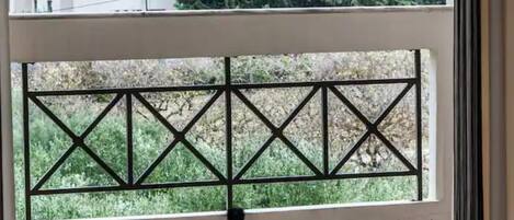 A table with a bottle and two glasses, a window with a view of buildings and trees, and a geometric metal railing.