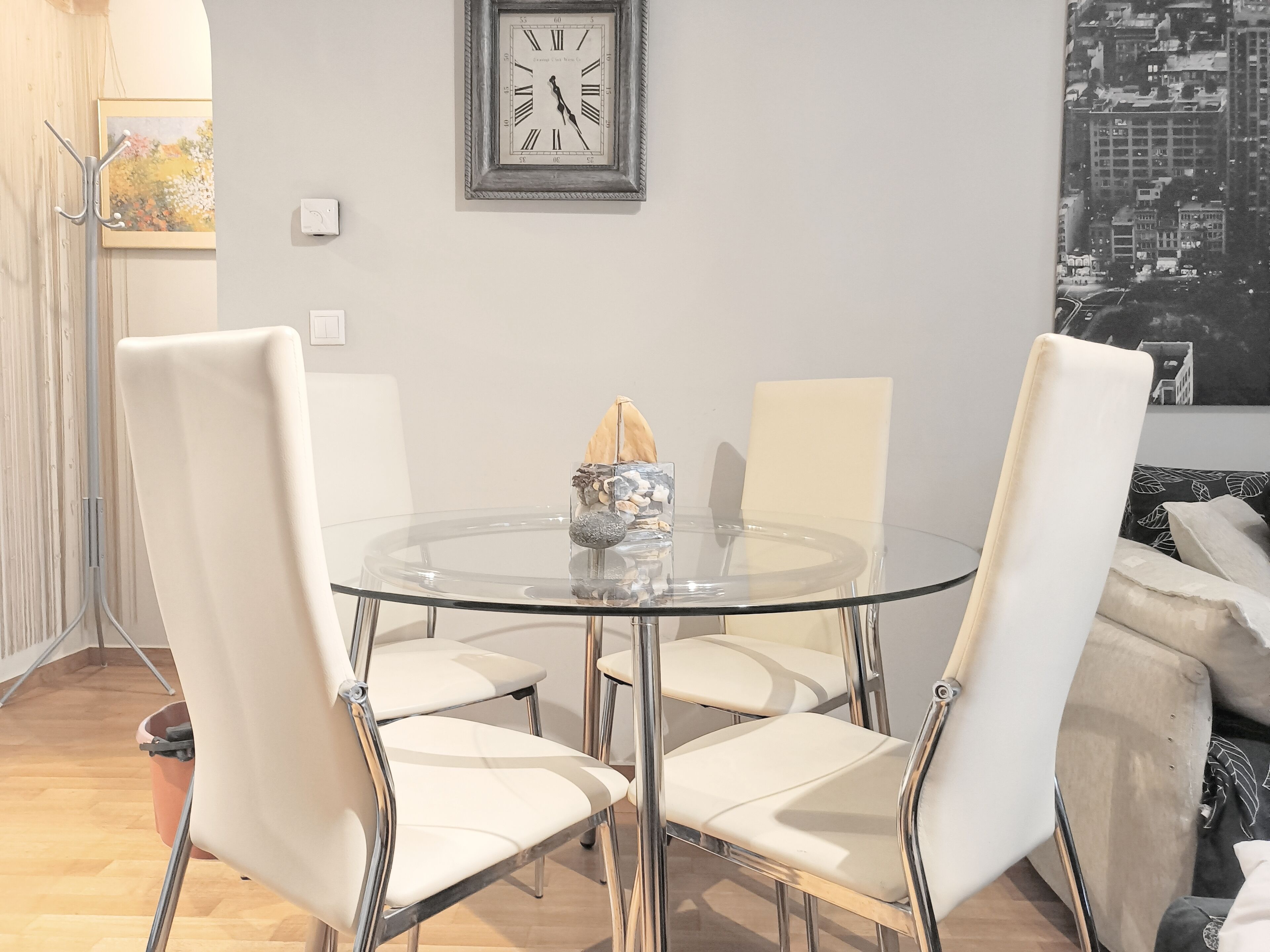 Un espace repas moderne avec une table ronde en verre, quatre chaises blanches et un vase décoratif.