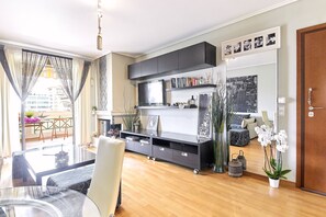 Un salon moderne avec une table à manger en verre, un canapé, un meuble de rangement noir pour appareils multimédias et un tableau représentant un paysage urbain.