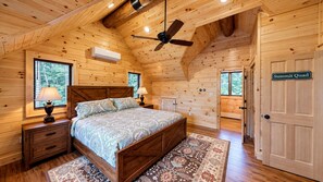 Une chambre dans une cabane en bois, avec un lit, des tables de chevet, un ventilateur de plafond et une fenêtre.
