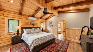 Een slaapkamer met een houten plafond, een bed met beddengoed met een patroon, een nachtkastje, een bijzettafeltje, een wandairconditioner en een deur naar een andere kamer.
