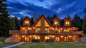 A large log cabin with multiple levels, outdoor lighting, and a stone chimney. - Grand Peaks Lodge, Luxury Log Home, Views, Hot Tub, Sauna, EV Charger, 3D Tour (Jay)