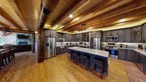 Une cuisine spacieuse dotée de meubles en bois foncé, d’appareils électroménagers en acier inoxydable et d’un grand îlot central avec des tabourets de bar.