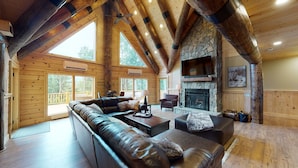 L’intérieur d’une cabane en rondins, avec une cheminée en pierre, des canapés en cuir et un grand téléviseur fixé au-dessus.