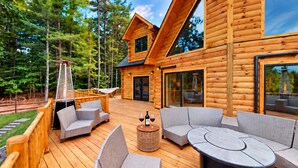 A wooden cabin with a deck, outdoor seating, and a glass door leading to the interior. - Grand Peaks Lodge, Luxury Log Home, Views, Hot Tub, Sauna, EV Charger, 3D Tour (Jay)