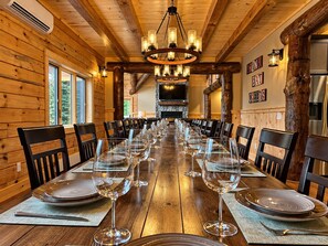A long wooden dining table set for a meal with chairs, a chandelier, and a stone fireplace in the background. - Grand Peaks Lodge, Luxury Log Home, Views, Hot Tub, Sauna, EV Charger, 3D Tour (Jay)