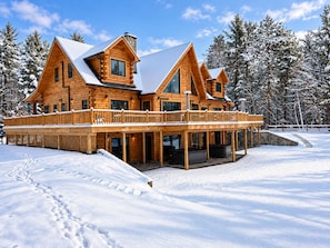 Une grande cabane en rondins à plusieurs niveaux, dotée d’un balcon, et entourée d’un paysage enneigé.