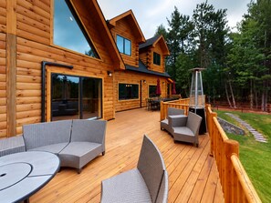 A wooden cabin with a deck, outdoor seating, and a staircase leading to a deck area. - Grand Peaks Lodge, Luxury Log Home, Views, Hot Tub, Sauna, EV Charger, 3D Tour (Jay)