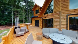 Une cabane en bois dotée d’une terrasse, de meubles en osier et d’un foyer extérieur.