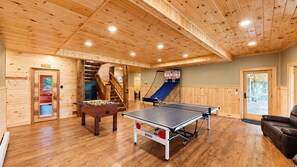 Ein Zimmer mit Holzboden, einer Tischfußballplatte, einem Pingpongtisch und einer Saunatür.