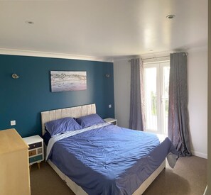 A bedroom with a bed, nightstands, a painting, and a window with curtains. - Outstanding 4 Bedroom Open-Plan Lodge.  (Newquay)