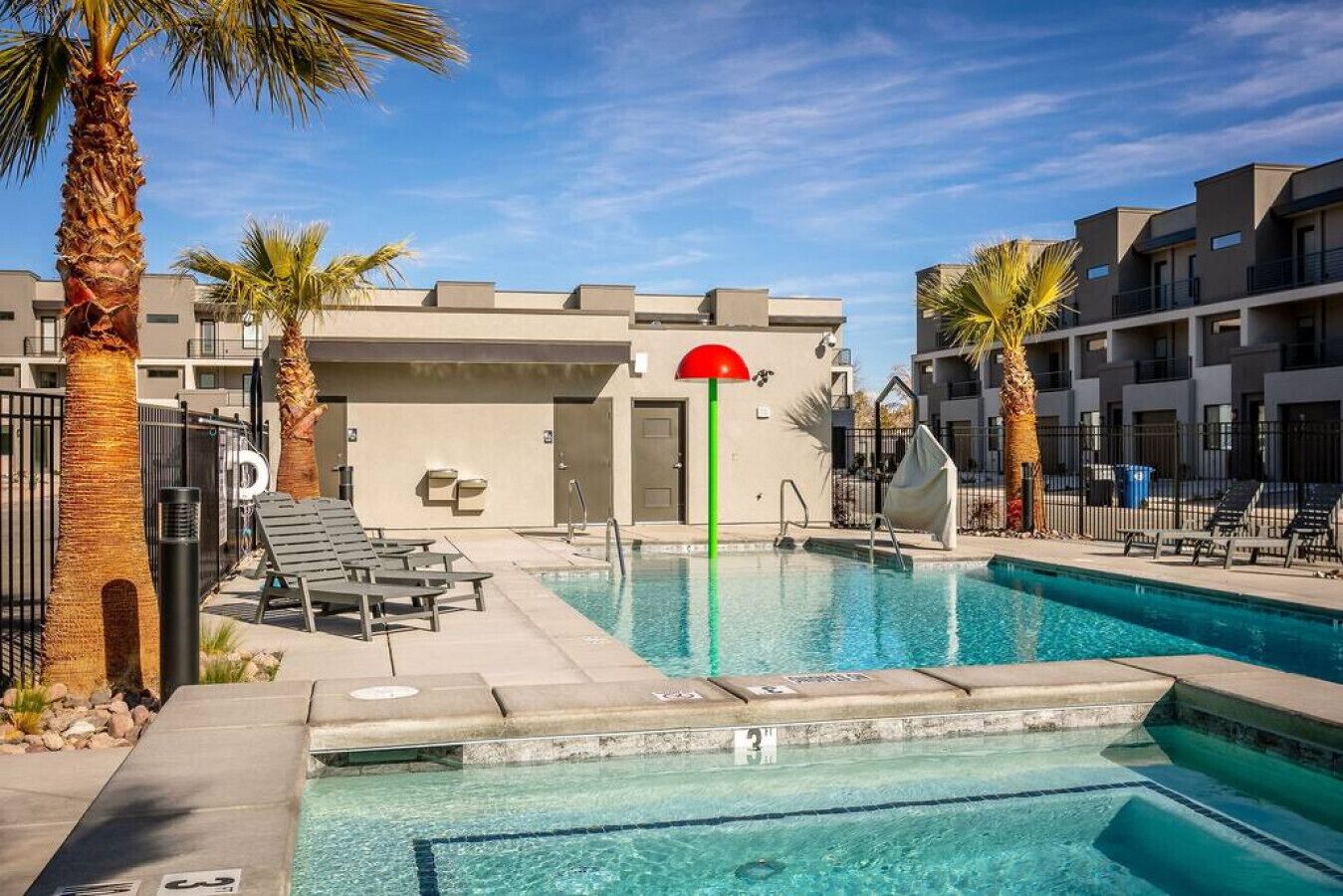 A swimming pool with lounge chairs and palm trees, surrounded by modern buildings.
