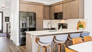 Une cuisine moderne avec des meubles en bois, des appareils électroménagers en acier inoxydable et un coin bar avec des tabourets.