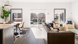 Un salon moderne avec un canapé, un coin repas comprenant une table et des chaises, et une grande porte-fenêtre coulissante donnant sur un espace extérieur.