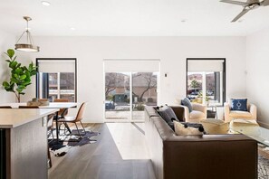 Een moderne woonkamer met een bank, een eethoek met een tafel en stoelen, en een grote schuifpui naar een buitenruimte.