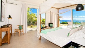 A bedroom with a bed, a desk, and a chair. There is a view of the ocean through large windows. - Aqua (4 bedrooms) - Ocean view villa with pool, Indigo Bay, St. Maarten (Indigo Bay)