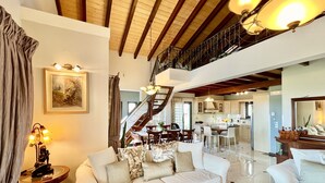 Un vaste espace de vie comprenant un canapé blanc, une table basse et un escalier menant à un niveau supérieur.