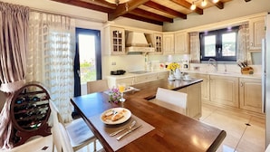 Une cuisine moderne avec des poutres en bois, un coin repas avec une table dressée pour deux personnes, et une vue sur l’extérieur.