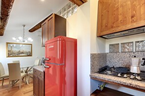 A compact kitchen with a red refrigerator, granite countertop, wooden cabinets, and a dining area with chairs.
