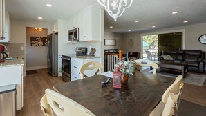 A modern kitchen with white cabinets, a stainless steel refrigerator, and a dining area with a wooden table and chairs. - Spacious 5 Bedroom - Sleeps 14 - Nintendo/Foosball/Games (Coeur d'Alene)