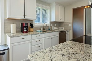 A modern kitchen with white cabinetry, a granite countertop, a coffee maker, and a window with blinds. - Spacious 5 Bedroom - Sleeps 14 - Nintendo/Foosball/Games (Coeur d'Alene)