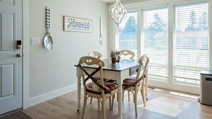 A dining area with a wooden table and chairs, a chandelier, and a window with blinds. - Spacious 5 Bedroom - Sleeps 14 - Nintendo/Foosball/Games (Coeur d'Alene)