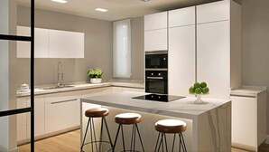 A modern kitchen with a central island, bar stools, a built-in oven, and a backsplash.