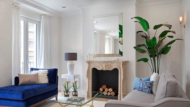 A living room with a blue sofa, a beige sofa, a glass coffee table, a fireplace, and a large mirror.