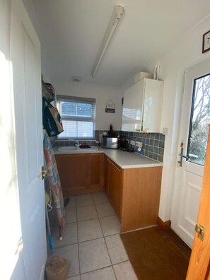 A compact kitchen with wooden cabinets, a countertop, and a window. - The Meadows St Teath, 4 bed sleeps 7 (Saint Teath)