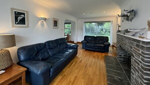 A spacious living room with a black leather sofa, a smaller sofa, a wooden coffee table, and a stone fireplace. - The Meadows St Teath, 4 bed sleeps 7 (Saint Teath)