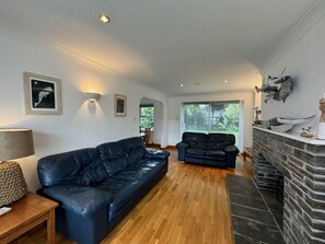 Ein geräumiges Wohnzimmer mit einer schwarzen Ledersofa, einem kleineren Sofa, einem Holztisch und einem Kamin aus Stein.