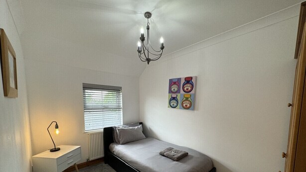 A small bedroom with a single bed, a desk, a chair, a radiator, a window with blinds, and a chandelier. - The Meadows St Teath, 4 bed sleeps 7 (Saint Teath)