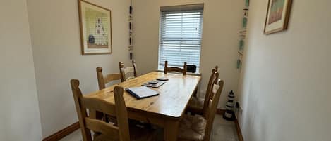 A dining room with a wooden table and chairs, a window with blinds, and a small decorative item on the wall.