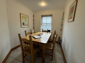 Ein Essbereich mit einem Holztisch und Stühlen, einem Fenster mit Jalousien und gerahmten Kunstwerken an den Wänden.