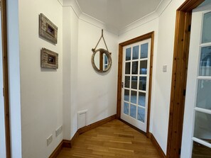 Ein Flur mit Holzdielen, einer weißen Tür mit Glasfenstern und einem runden Spiegel an der Wand.