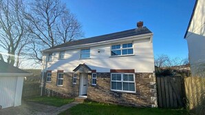 A two-story house with a stone facade, a front porch, and a small garage. - The Meadows St Teath, 4 bed sleeps 7 (Saint Teath)