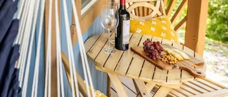 Een hangmat, houten stoelen, een klein tafeltje met een fles wijn, een glas, druiven en een houten plank met mais.