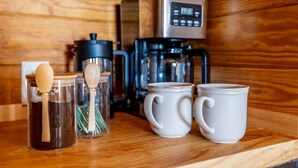 Una encimera de cocina con una cafetera, dos tazas y un tarro con una cuchara de madera.