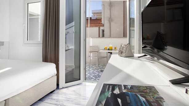 A hotel room with a bed, a desk, a chair, a small table with drinks, and a window with a view of buildings.