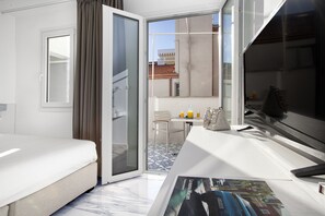 Ein Hotelzimmer mit Bett, Schreibtisch, Stuhl, einem kleinen Tisch mit Getränken und einem Fenster mit Blick auf Gebäude.