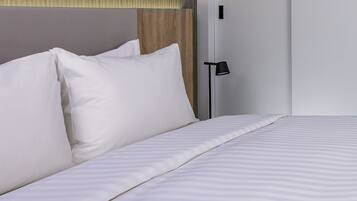 A neatly made bed with white bedding and pillows, a wooden headboard, and a black floor lamp.