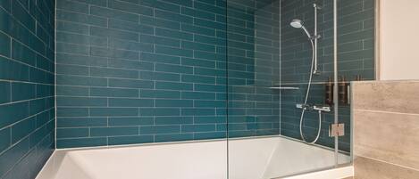 A modern bathroom with a glass-enclosed bathtub, teal blue tiles, and a beige tiled shower area.