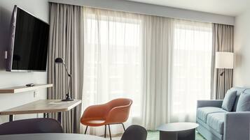 A modern hotel room with a flat-screen TV, a desk with a chair, a sofa, and a round coffee table.