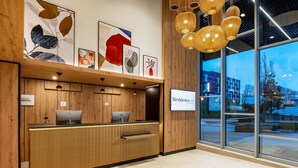 A hotel reception desk with a wooden finish, a computer, and a sign for 'Residence Inn'. - Residence Inn by Marriott Paris Charles de Gaulle Airport (Roissy-en-France)