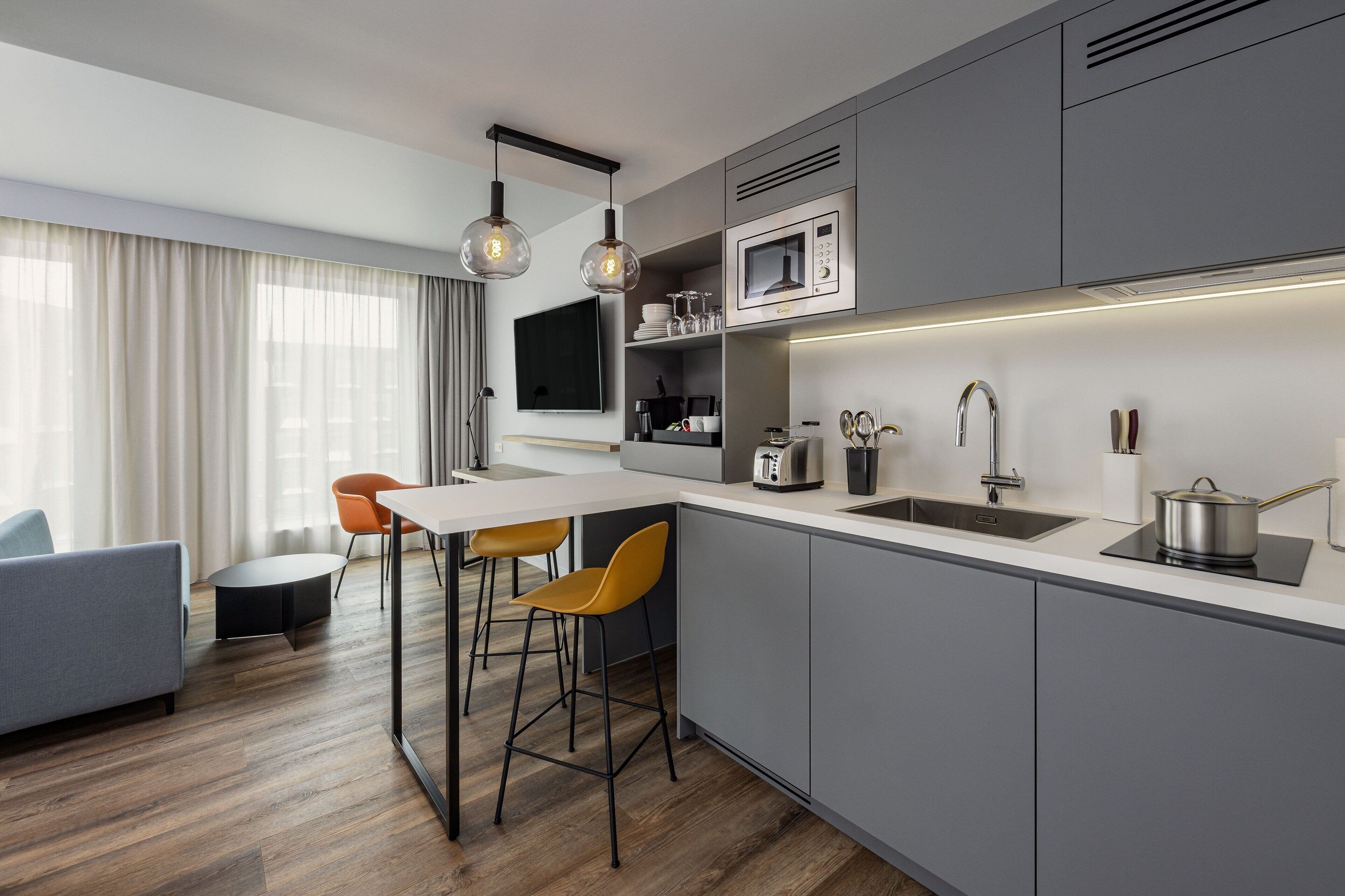 A modern kitchen with a central island, bar stools, a microwave, and a sink.