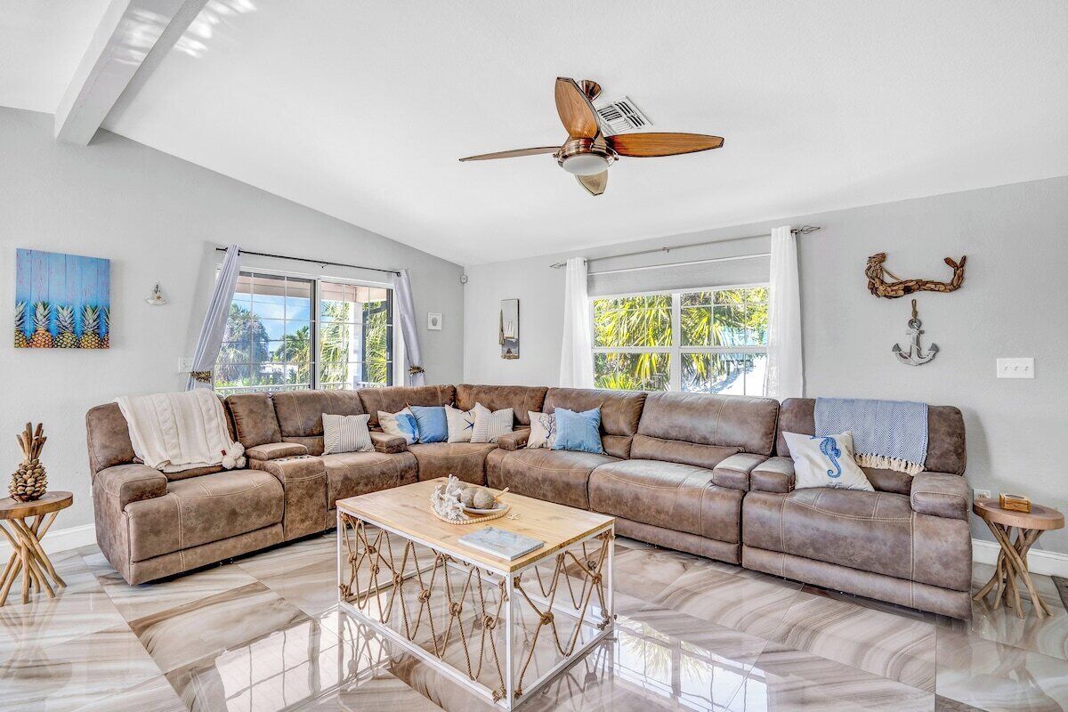 A spacious living room with a large brown leather sectional sofa, a wooden coffee table, and a ceiling fan.