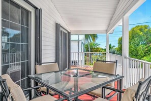 A glass-top table with four chairs on a covered porch with white railings.