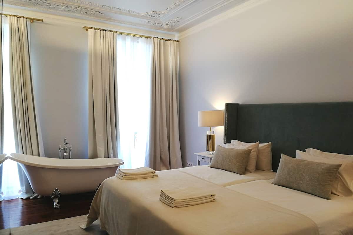 Una habitación de hotel con una cama grande, una bañera y una mesita de noche con una lámpara.